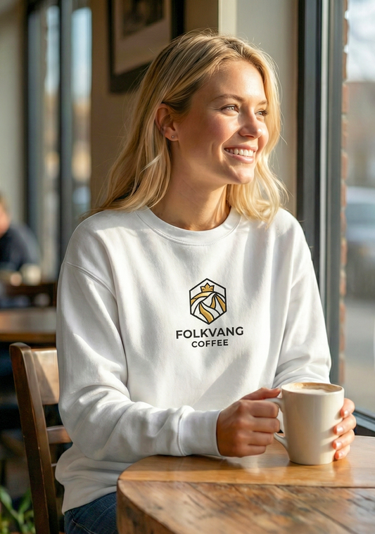 Woman wearing a white sweatshirt with Folkvang Coffee logo, holding a coffee mug indoors.